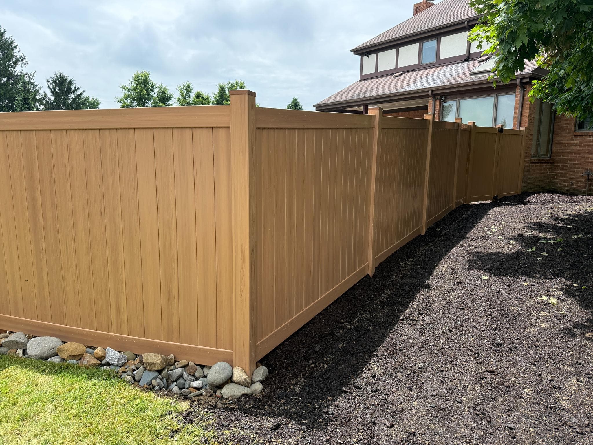 Cedar-tone vinyl privacy fence running alongside a Pittsburgh home