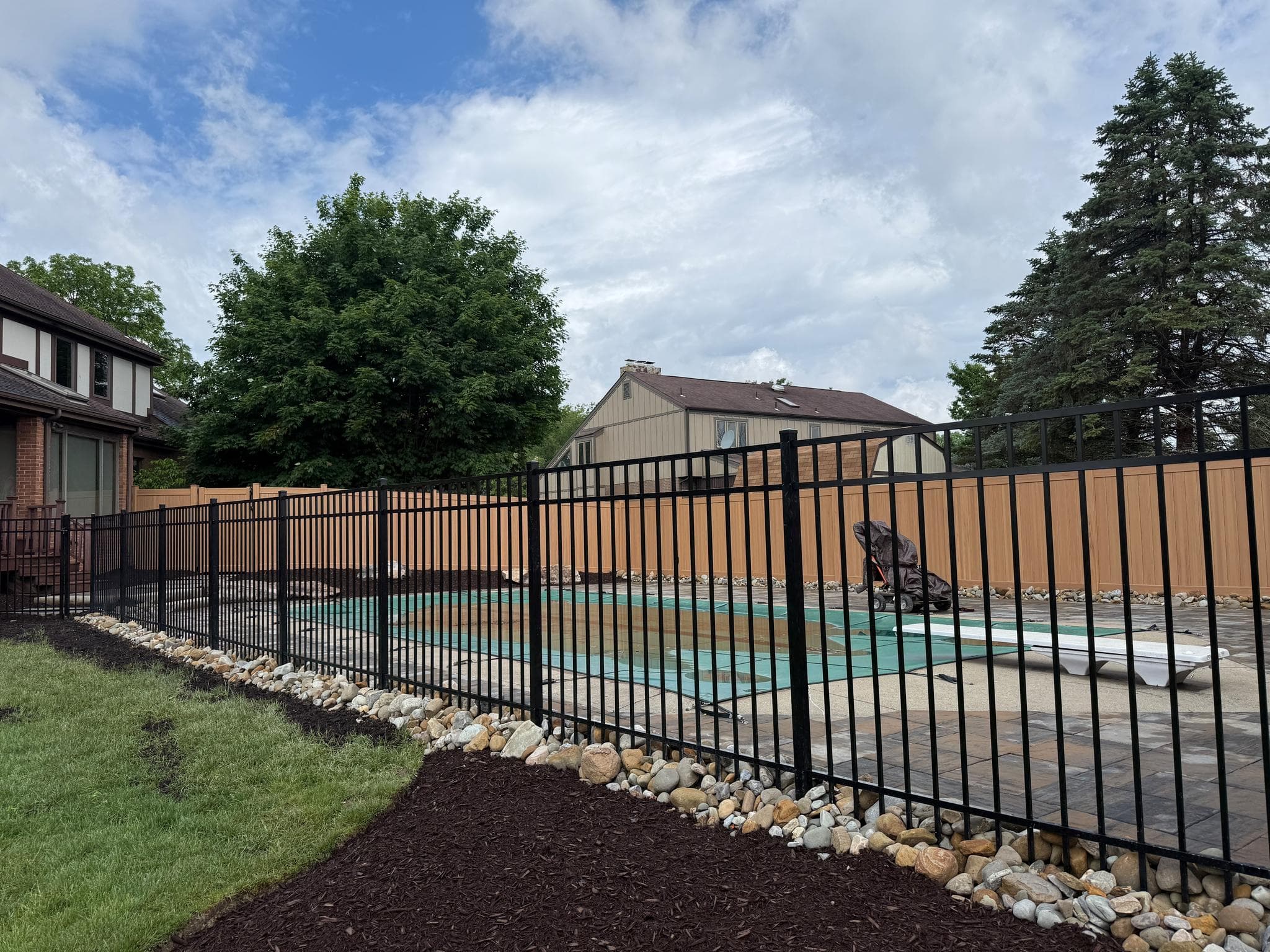 Aluminum pool safety fence enclosing a Pittsburgh backyard pool with a river-rock border