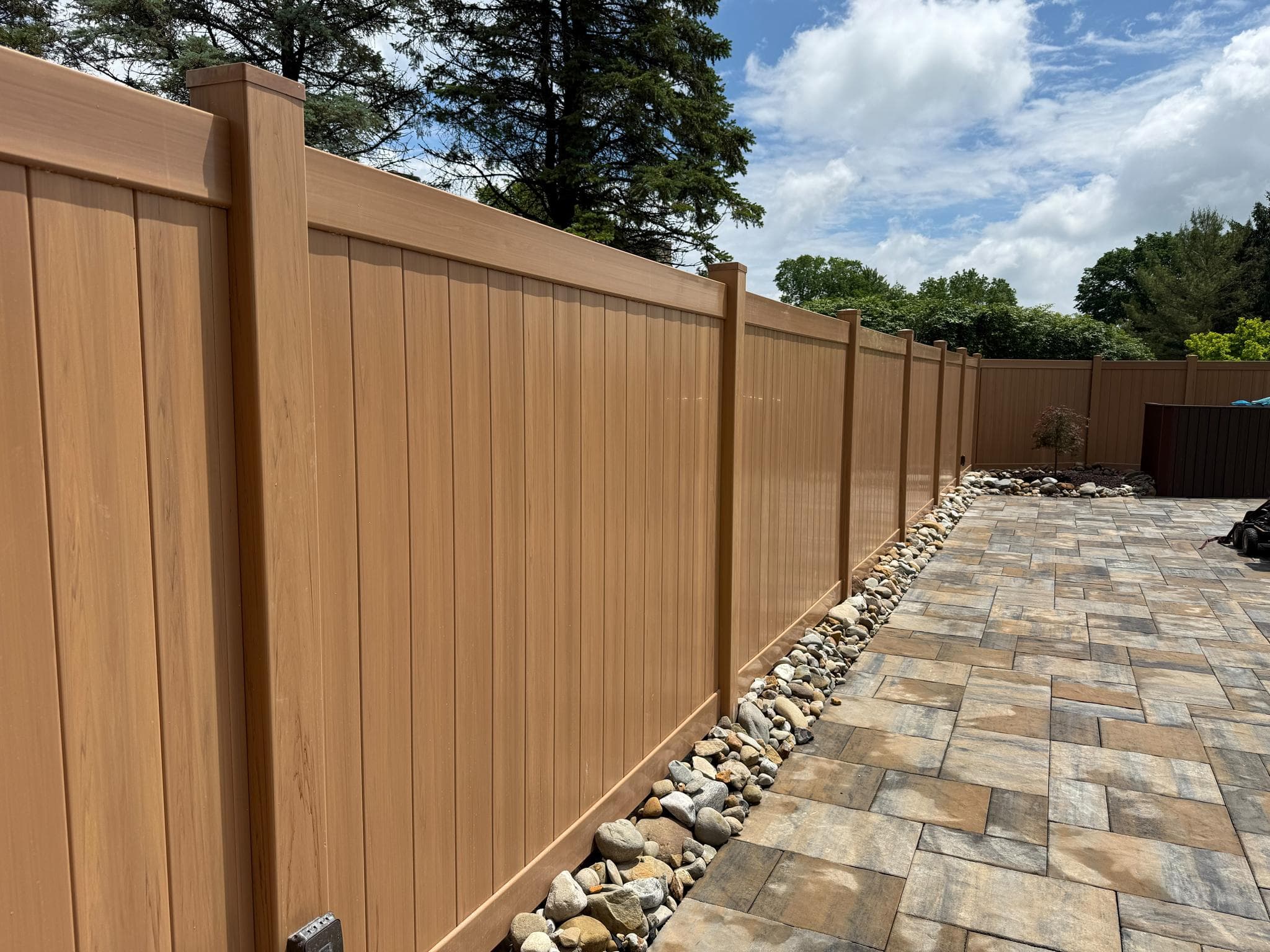 Cedar-tone vinyl privacy fence beside a paver patio in Pittsburgh